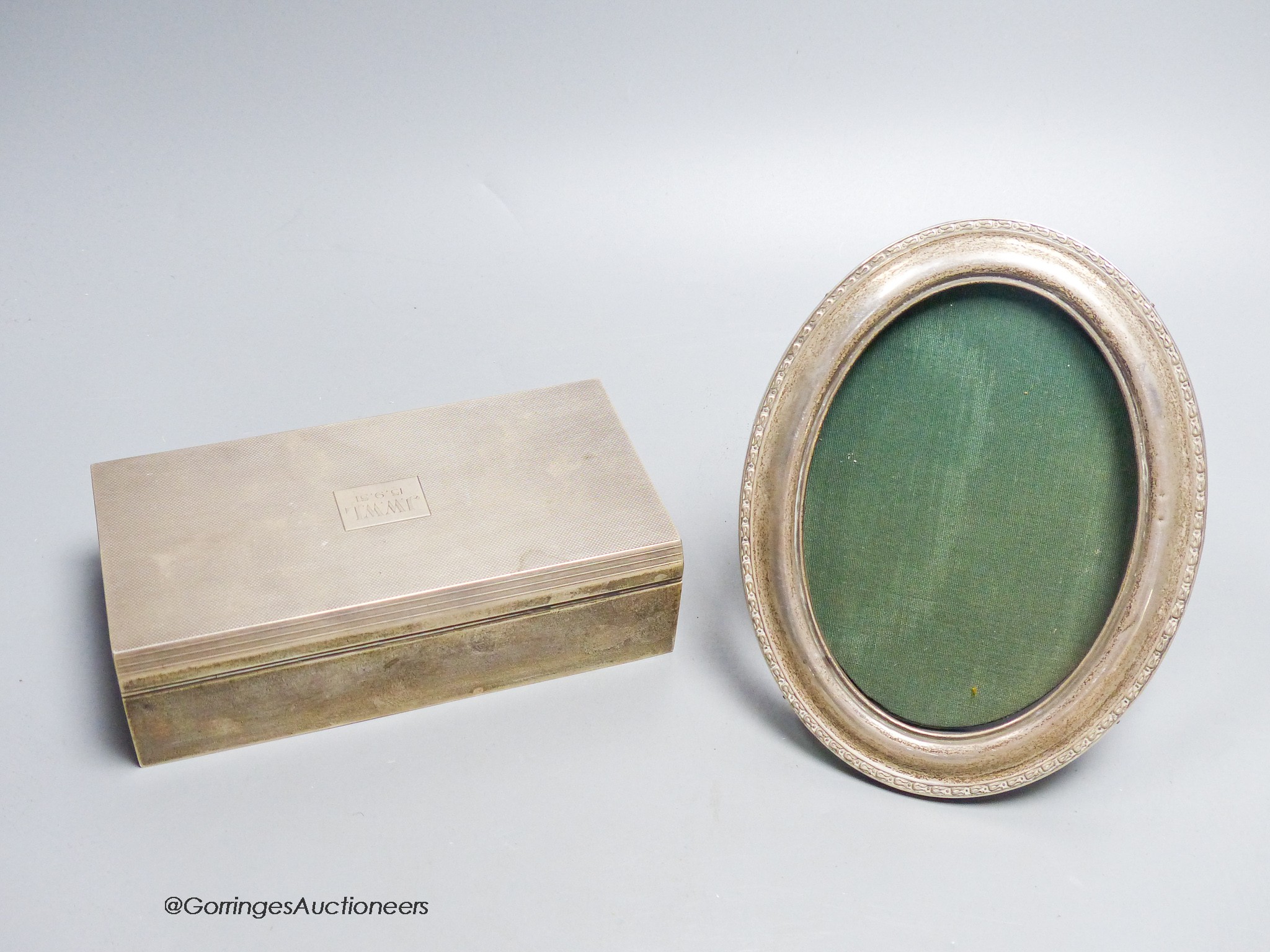 A 1940's engine turned rectangular silver mounted cigarette box, with engraved inscription, 17cm and a silver mounted oval photograph frame.